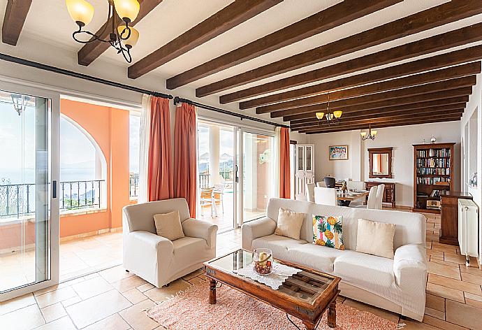 Open-plan living room with sofas, dining areas, kitchen, ornamental fireplace, WiFi internet, satellite TV, and terrace access with panoramic sea views . - Villa Emilios . (Photo Gallery) }}