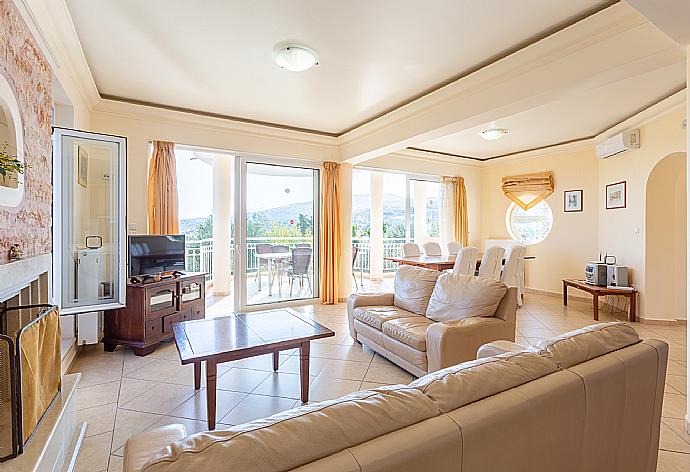 Open-plan living room with sofas, dining area, kitchen, ornamental fireplace, A/C, WiFi internet, satellite TV, DVD player, and balcony access . - Villa Asimenia . (Fotogalerie) }}