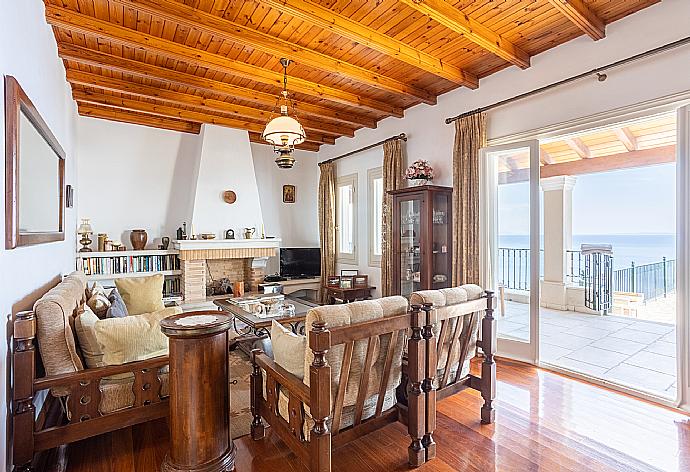 Open-plan living room with sofas, dining area, kitchen, ornamental fireplace, A/C, WiFi internet, satellite TV, and terrace access with sea views . - Villa Elpida . (Fotogalerie) }}