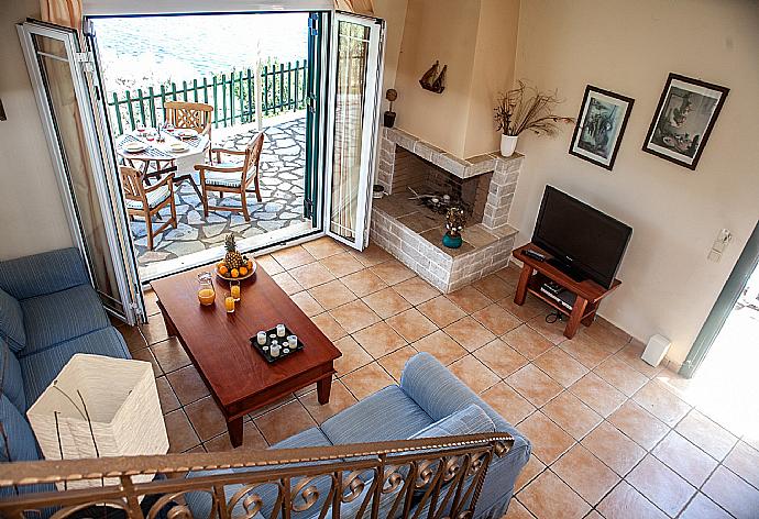 Open-plan living room with sofas, dining area, kitchen, ornamental fireplace, A/C, WiFi internet, satellite TV, and terrace access with sea views . - Villa Flisvos . (Fotogalerie) }}