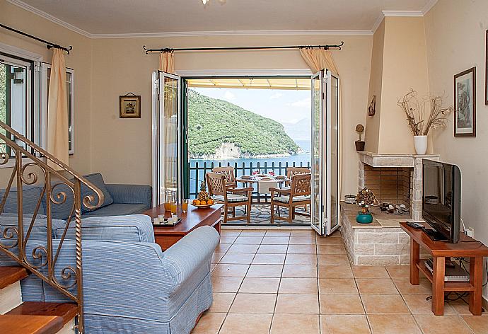 Open-plan living room with sofas, dining area, kitchen, ornamental fireplace, A/C, WiFi internet, satellite TV, and terrace access with sea views . - Villa Flisvos . (Fotogalerie) }}