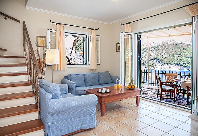 Open-plan living room with sofas, dining area, kitchen, ornamental fireplace, A/C, WiFi internet, satellite TV, and terrace access with sea views . - Villa Flisvos . (Fotogalerie) }}