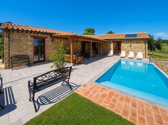 ,A rustic stone villa with a terracotta roof features a covered patio and a sparkling blue swimming pool. White lounge chairs and a black metal bench sit on a light grey tiled patio under a clear blue sky. . - Villa Il Melograno . (Photo Gallery) }}
