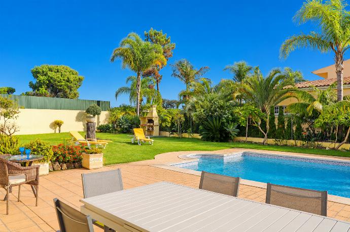 A poolside view featuring a spacious patio with dining furniture in the foreground, looking across a swimming pool toward a lawn with palm trees and a brick barbecue grill. . - Villa Green Palms . (Photo Gallery) }}
