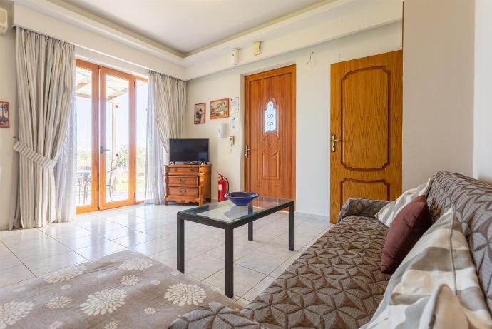 Open-plan living room with sofa, dining area, kitchen, A/C, WiFi internet and satellite TV, and terrace access . - Maroulas Villas Collection . (Fotogalerie) }}