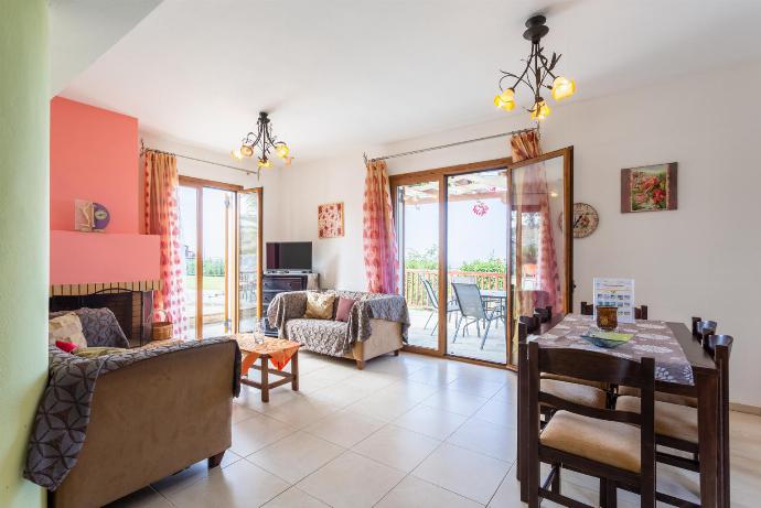 Open-plan living room with sofa, dining area, kitchen, A/C, WiFi internet and satellite TV, and terrace access . - Maroulas Villas Collection . (Fotogalerie) }}