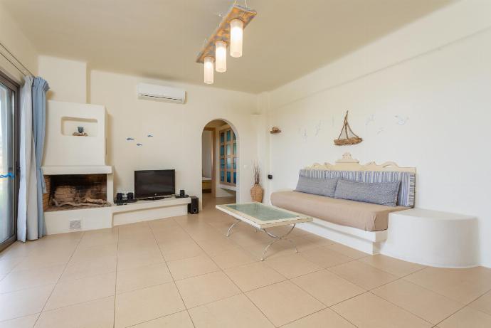 Open-plan living room with sofa, dining area, kitchen, ornamental fireplace, A/C, WiFi internet, satellite TV, and terrace access . - Panormos Villas Collection . (Fotogalerie) }}