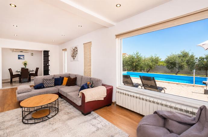 This bright, modern living room features a brown sectional sofa and a wooden coffee table facing a large picture window that overlooks a crystal-blue swimming pool. . - Villa Maslina . (Photo Gallery) }}