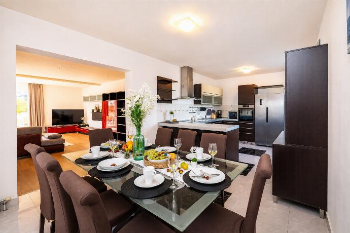 A modern open-plan dining and kitchen area features a glass-top dining table set for six with brown upholstered chairs, opening up to a contemporary kitchen with dark wood cabinets and stainless steel appliances. . - Villa Maslina . (Photo Gallery) }}