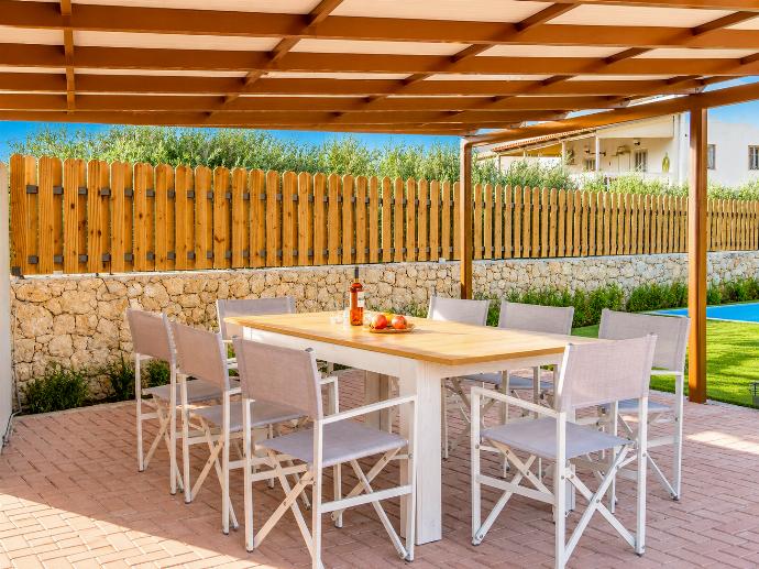 Shaded outdoor dining area with a wooden pergola, modern seating, and a sunny garden setting. . - Villa Galini . (Galería de imágenes) }}