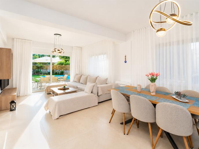 Bright open-plan living and dining area with elegant white decor, modern lighting, and direct access to the private pool terrace. . - Villa Galini . (Galería de imágenes) }}