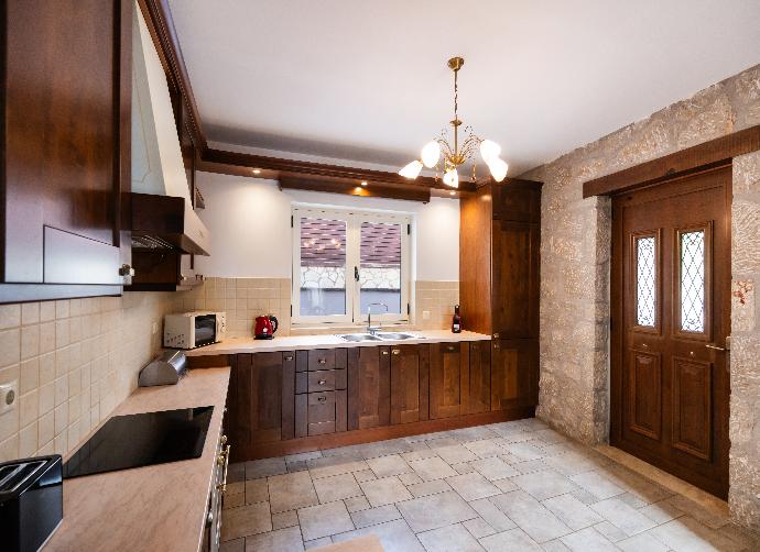 Kitchen area with rich wooden cabinets, tiled floors, and a stone wall accent. . - Villa Galatia . (Photo Gallery) }}