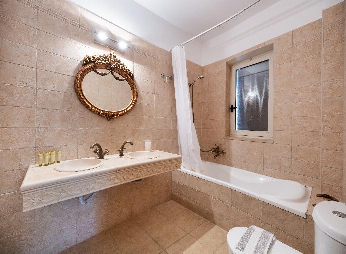 Beige tiled bathroom featuring a built-in bathtub, a vanity sink, and an ornate gold mirror. . - Villa Galatia . (Photo Gallery) }}