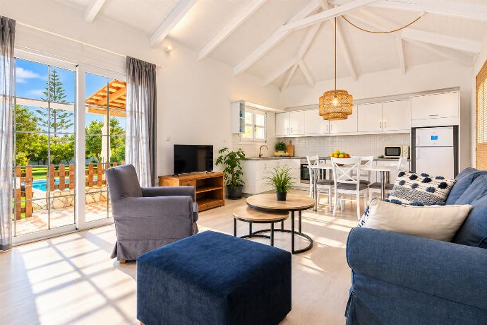 Bright open-plan lounge and dining area with comfortable sofas, modern TV, vaulted ceiling, and abundant natural light.