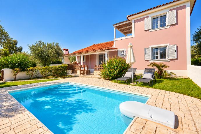 Attractive villa with a private swimming pool, stone terrace, sun loungers, and colourful garden surroundings.