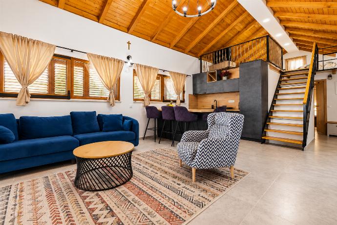 Rustic open-plan living and dining area with blue sofas, exposed wooden ceiling, stone details, and warm contemporary furnishings.