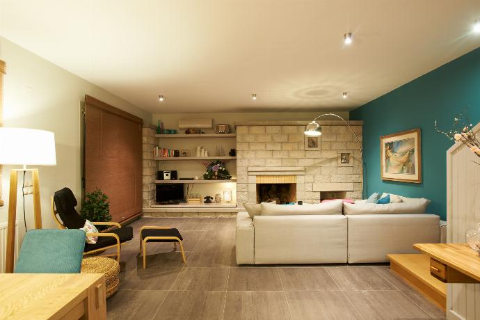 A bright living space features a grey sectional sofa facing a stone fireplace, built-in shelving with a television, and large glass sliding doors that look outside. . - Villa Santolina . (Galerie de photos) }}