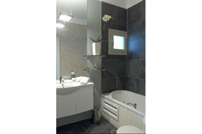 A contemporary bathroom features dark slate-look tiling over a jetted bathtub paired with a white floating vanity and a large wall mirror. . - Villa Santolina . (Galerie de photos) }}