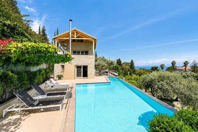 A patio view showcases lounge chairs lining a bright blue swimming pool next to a multi-story stone villa, offering a panoramic outlook toward the distant sea. . - Villa Oleana . (Galería de imágenes) }}