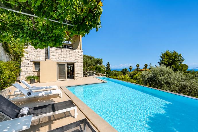 An outdoor swimming pool is bordered by lounge chairs and a stone villa patio, offering a sweeping view of green treetops and the sea beyond. . - Villa Oleana . (Galería de imágenes) }}