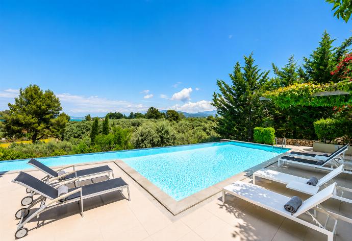 An expansive outdoor swimming pool is surrounded by lounge chairs on a spacious tiled deck, overlooking a vast landscape of green trees under a bright blue sky. . - Villa Oleana . (Galería de imágenes) }}