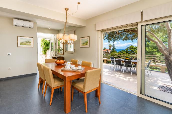 A wooden dining table paired with upholstered chairs is lit by a classic chandelier, situated next to large sliding glass doors that open to an outdoor terrace with a sea view. . - Villa Oleana . (Galería de imágenes) }}