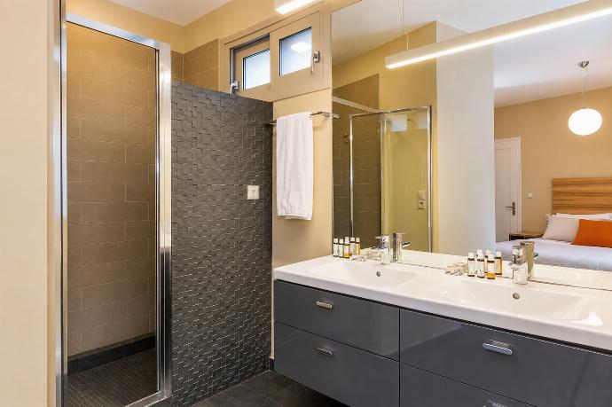 A modern bathroom features a glass-enclosed shower with dark mosaic tiling, a large floating grey vanity with double sinks, and a wide mirror reflecting an adjacent bedroom. . - Villa Oleana . (Galería de imágenes) }}