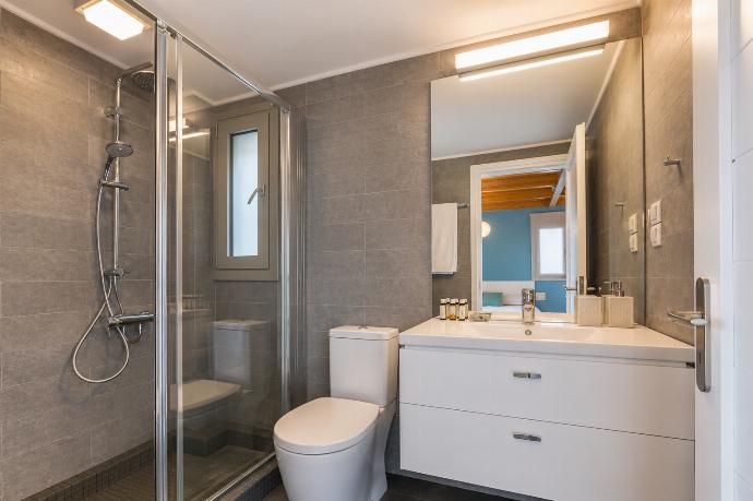 A contemporary bathroom features grey wall tiles, a glass-enclosed walk-in shower, a white vanity with drawers, and a large mirror reflecting an adjacent bedroom. . - Villa Oleana . (Galería de imágenes) }}