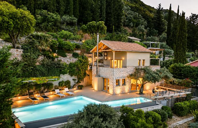 An elevated view showcases a multi-level hillside villa illuminated at dusk, featuring a private swimming pool, terrace spaces, and surrounding green forest. . - Villa Oleana . (Galería de imágenes) }}