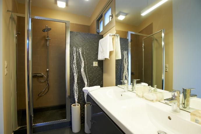 A modern bathroom features a glass-enclosed shower with dark mosaic tiling, a large floating grey vanity with double sinks, and a wide mirror reflecting an adjacent bedroom. . - Villa Oleana . (Galerie de photos) }}