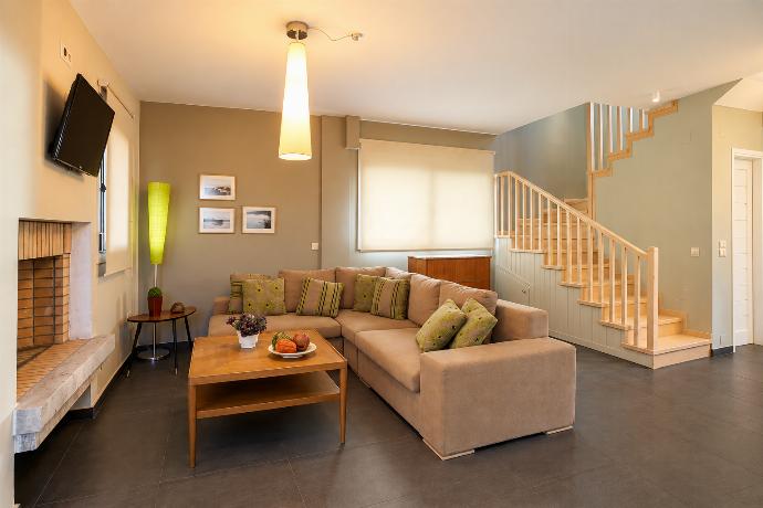 A spacious open-plan living room features a beige sectional sofa with red accent pillows, a wooden coffee table, a staircase, and a dining area in the background.