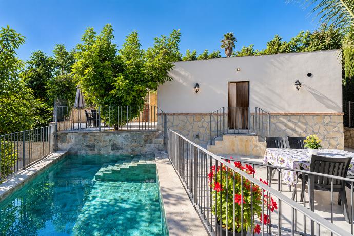 Private swimming pool with wide entry steps, outdoor dining terrace, stone detailing, and lush Mediterranean garden surroundings.