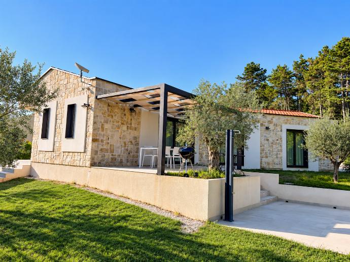 Traditional stone villa exterior with a shaded pergola terrace, outdoor seating, and landscaped garden surroundings.