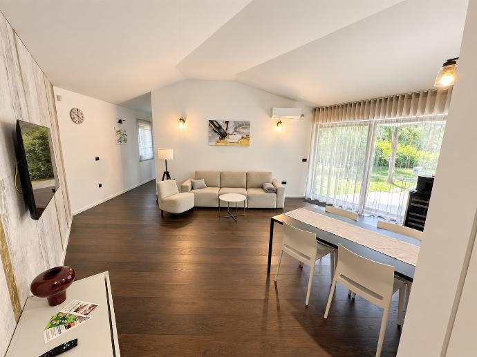 Bright open-plan living and dining room with modern furnishings, wooden flooring, and large windows overlooking the garden.