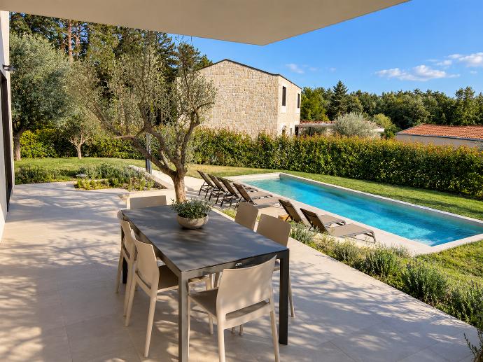 Outdoor dining terrace overlooking the private swimming pool, sun loungers, and landscaped Mediterranean garden.