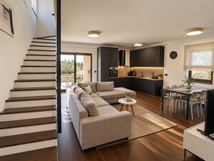 Spacious open-plan living and kitchen area with comfortable seating, modern furnishings, and warm wooden flooring.