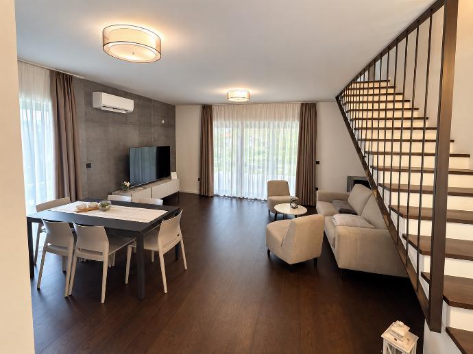 Spacious contemporary lounge and dining room with large windows, comfortable sofas, modern decor, and warm wooden flooring.