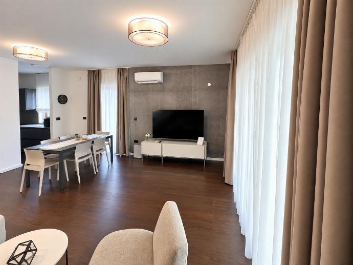 Modern living area with comfortable seating, dining space, wall-mounted TV, and plenty of natural light.