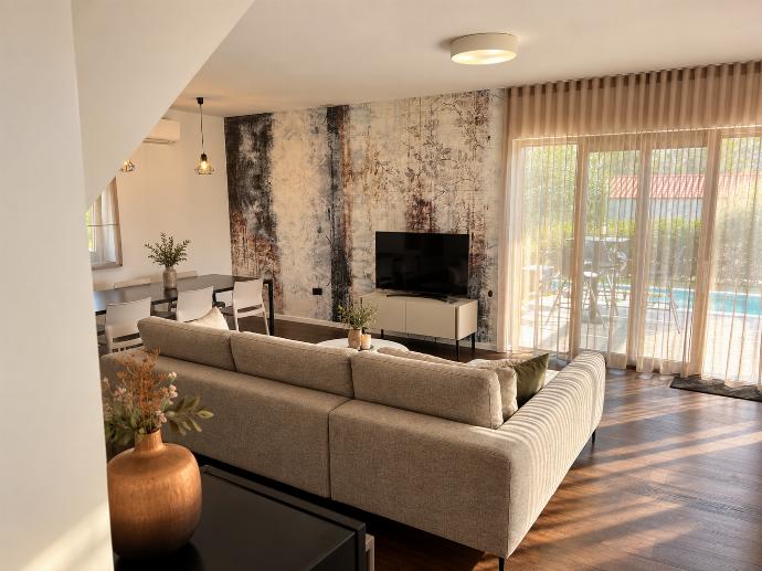 Spacious living room with a large corner sofa, wall-mounted TV, natural light, and stylish feature walls.