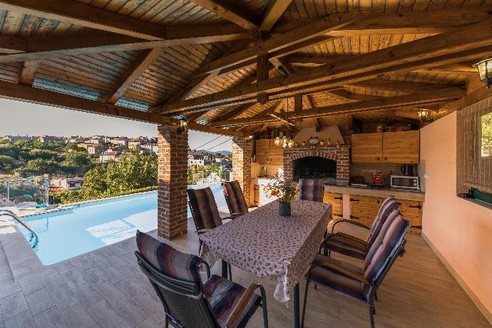 Outdoor kitchen and dining space with a built-in barbecue and rustic wooden ceiling