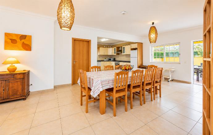 Spacious dining area with a large wooden table, open-plan kitchen, contemporary lighting, and bright neutral decor.