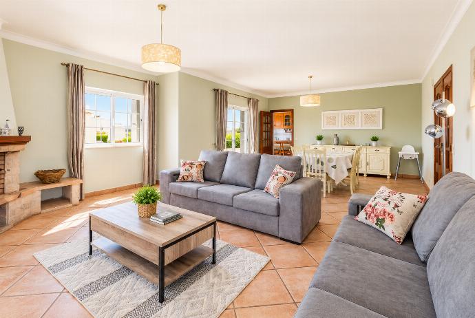 Bright living room with comfortable sofas, coffee table, tiled flooring, and large windows overlooking the outdoor area.
