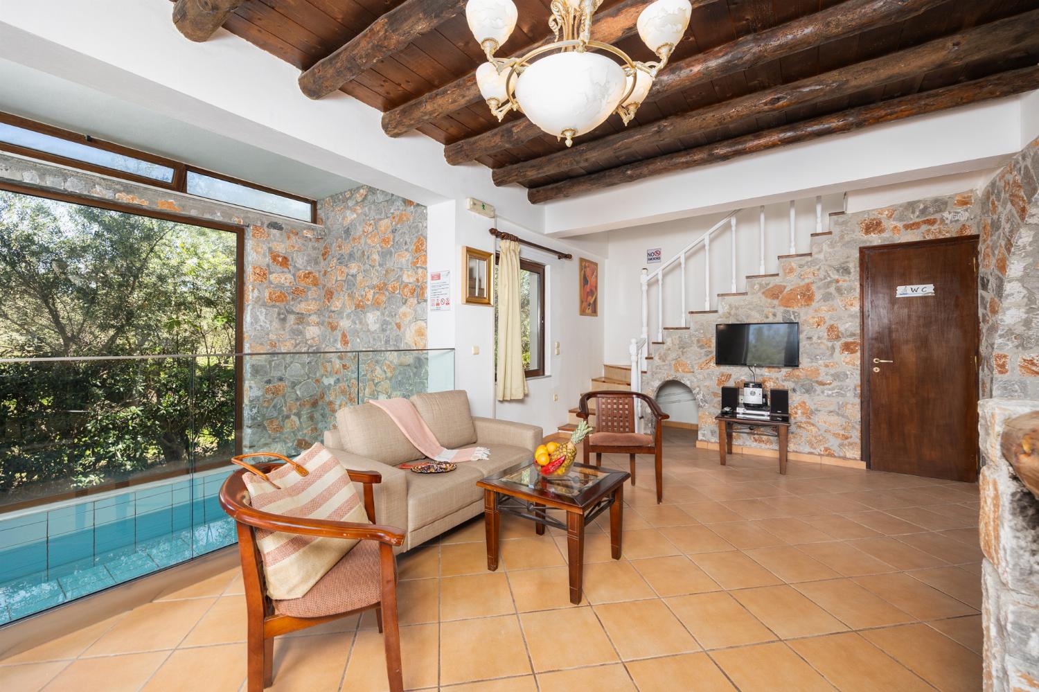 Open-plan living room with sofa, dining area, kitchen, indoor pool, ornamental fireplace, A/C, WiFi internet, and satellite TV