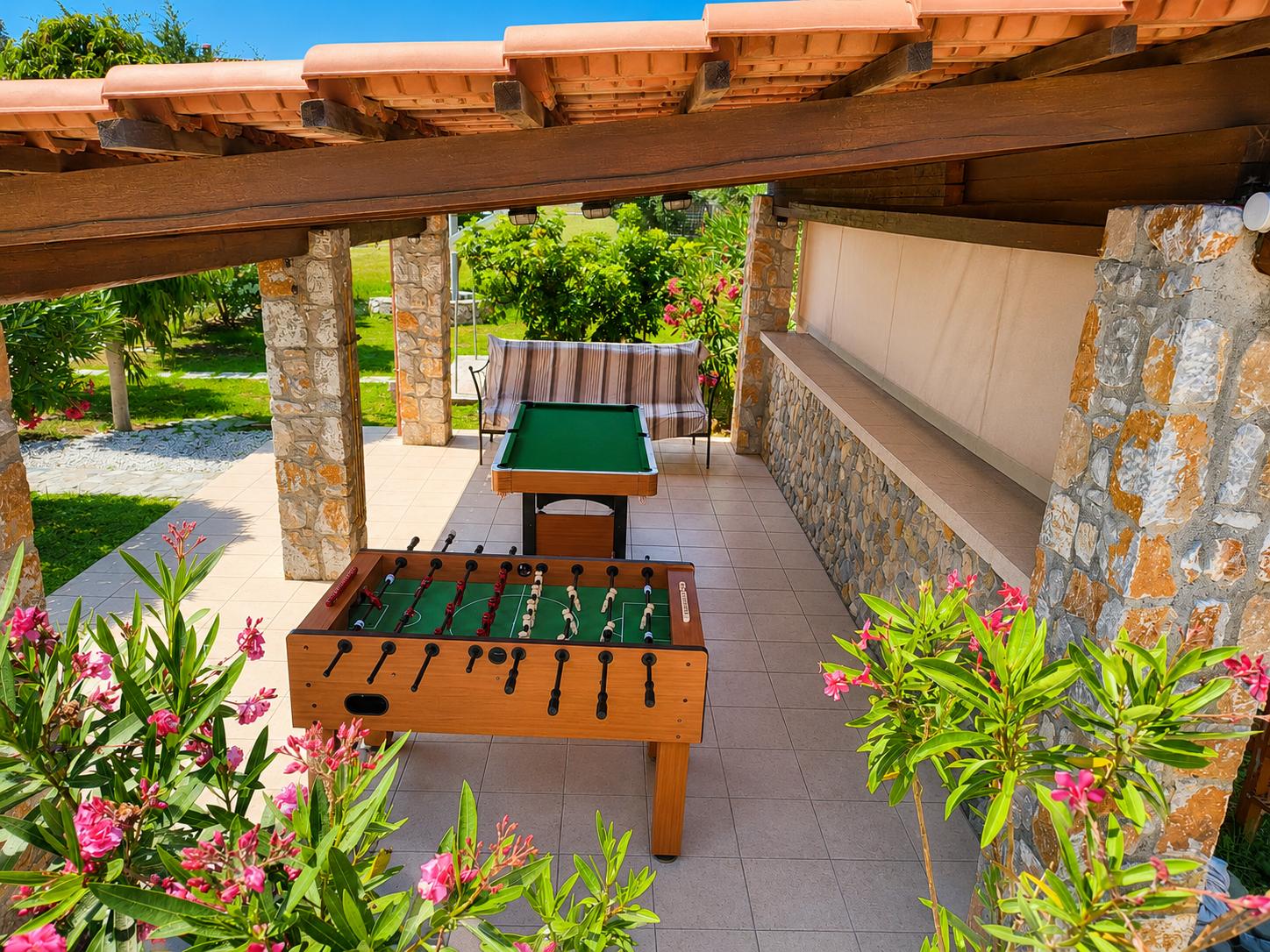 Covered outdoor games area with table football, pool table, and lush garden surroundings.