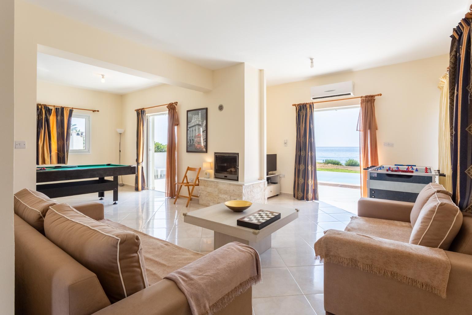 Open-plan living room with sofas, dining area, kitchen, ornamental fireplace, A/C, WiFi internet, satellite TV, pool table, foosball table, and terrace access with sea views