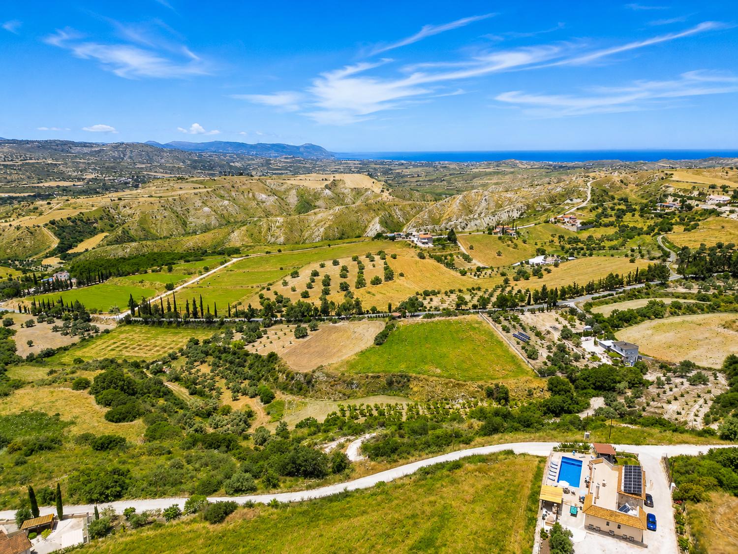Panoramic countryside landscape with rolling hills, distant sea views, and a bright blue sky.