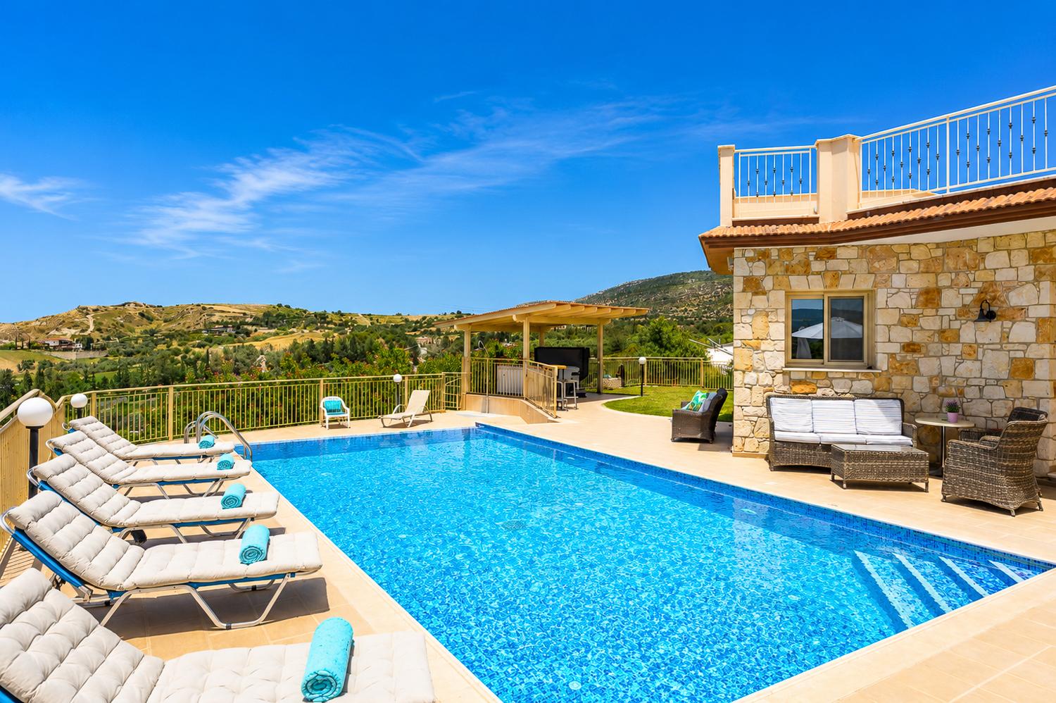Sunny private pool area with comfortable sun loungers, a stone villa backdrop, and beautiful countryside views.