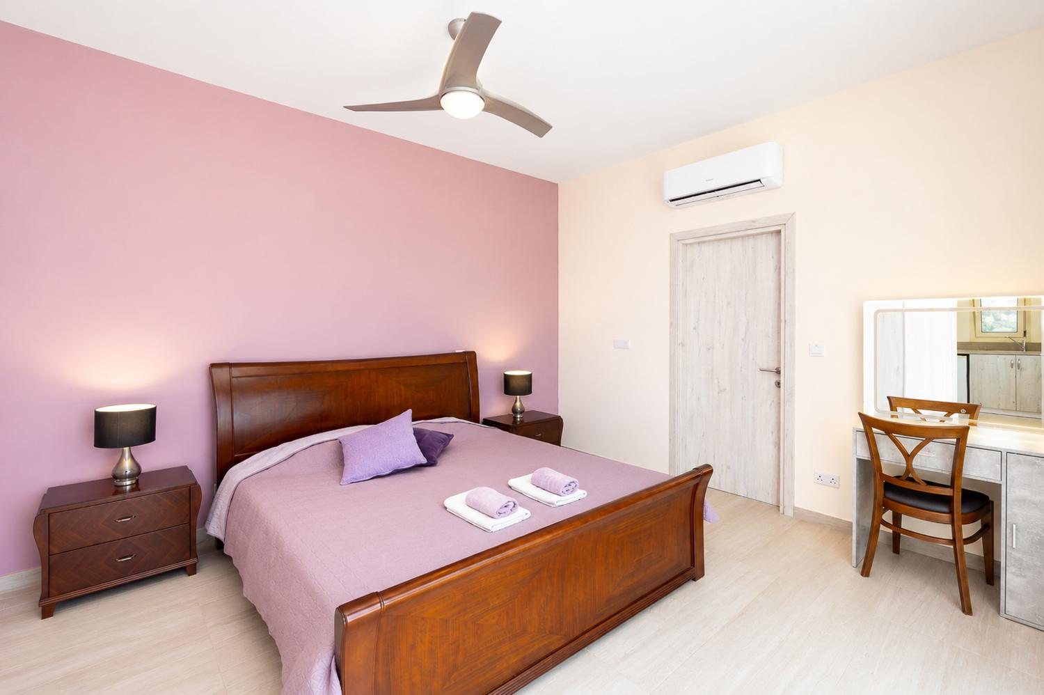 Bright double bedroom with soft purple tones, wooden furniture, and a modern dressing area.
