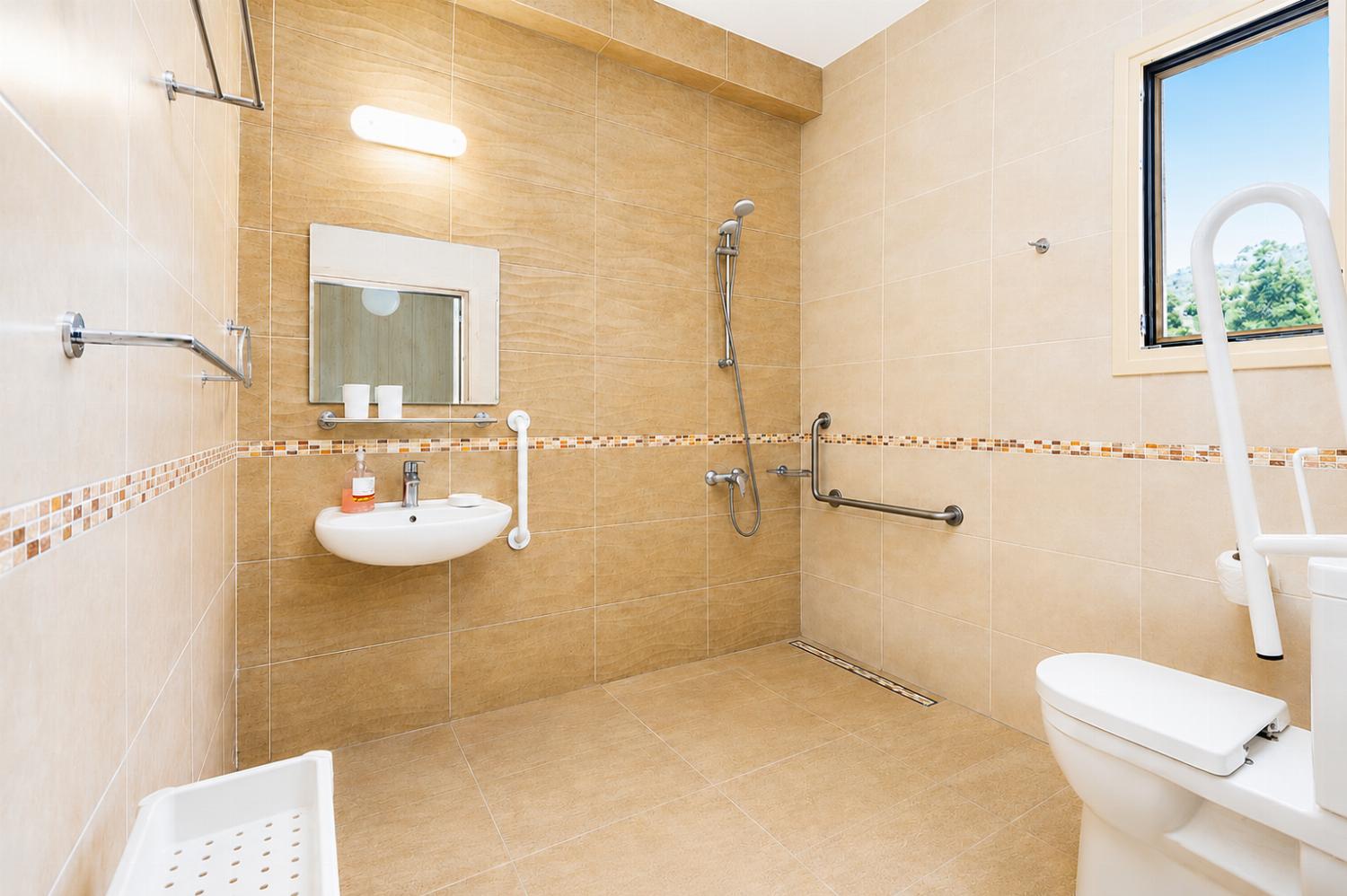 Accessible bathroom with a spacious walk-in shower, support rails, and bright modern tiling.
