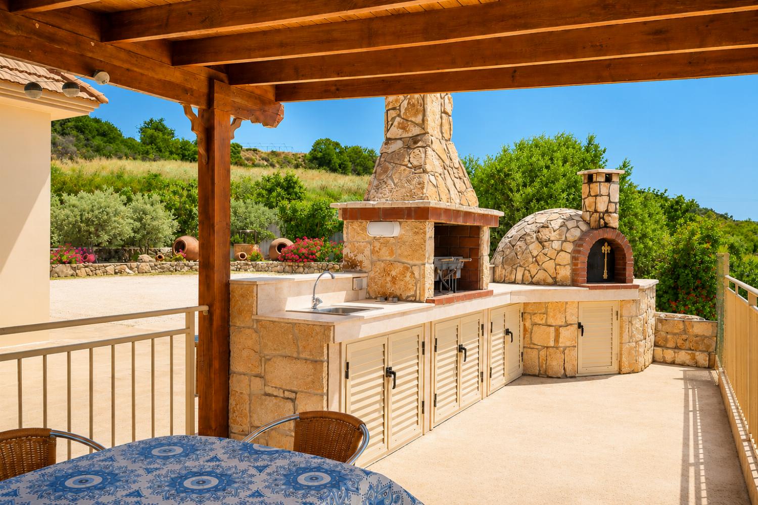 Covered outdoor BBQ area with stone oven, dining space, and beautiful countryside surroundings.